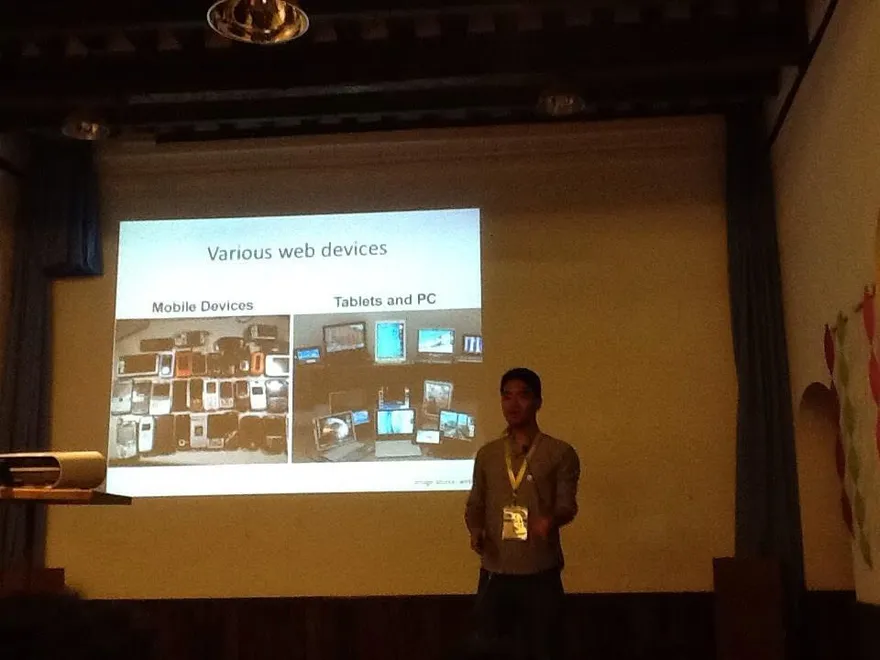 A speaker on stage beside a slide titled ‘Various web devices’, showing phones, tablets and computers.