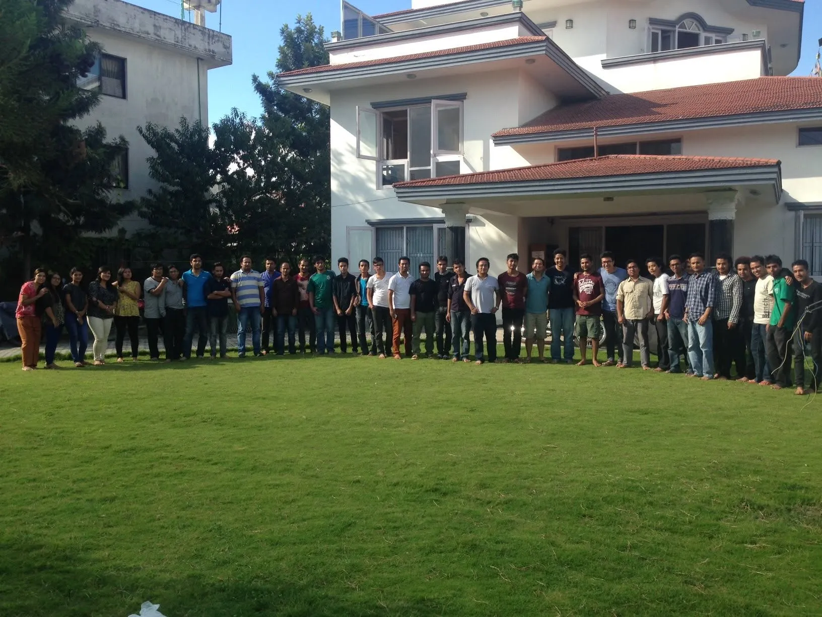 A large group from LastDoor standing in a long line on the lawn of the LastDoor office, a white house with a red tiled roof.