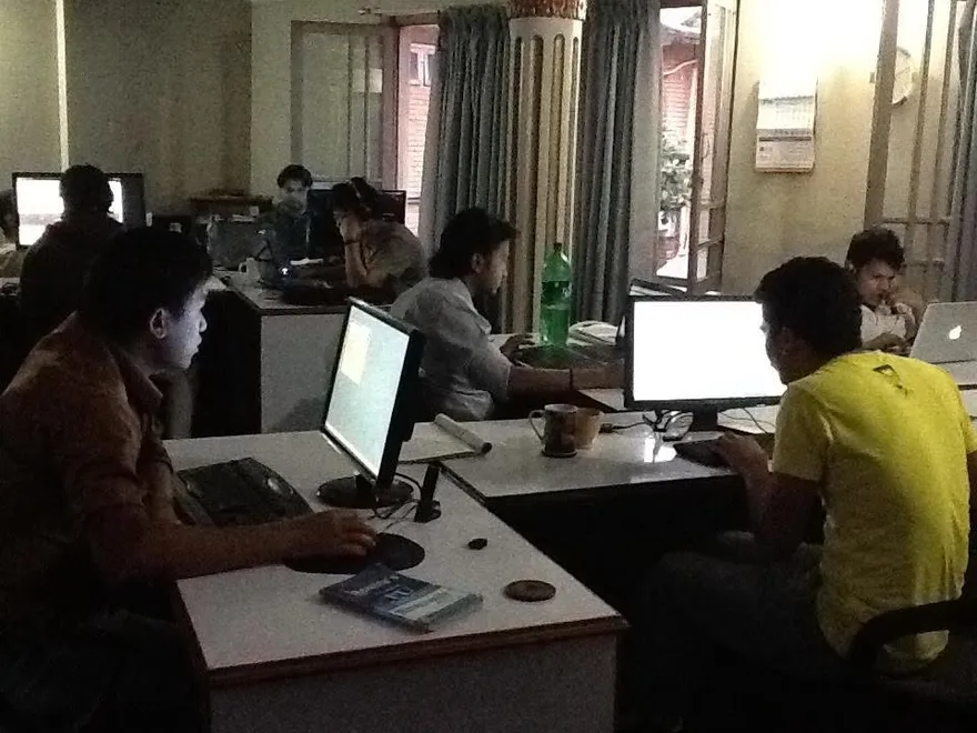 People working at desks in a dim office in the evening, lit by their screens.